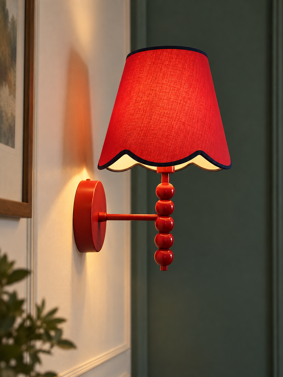 PROMIN red beaded wall sconce with scalloped red fabric shade and navy trim, lit on a cream wall next to dark green paneling