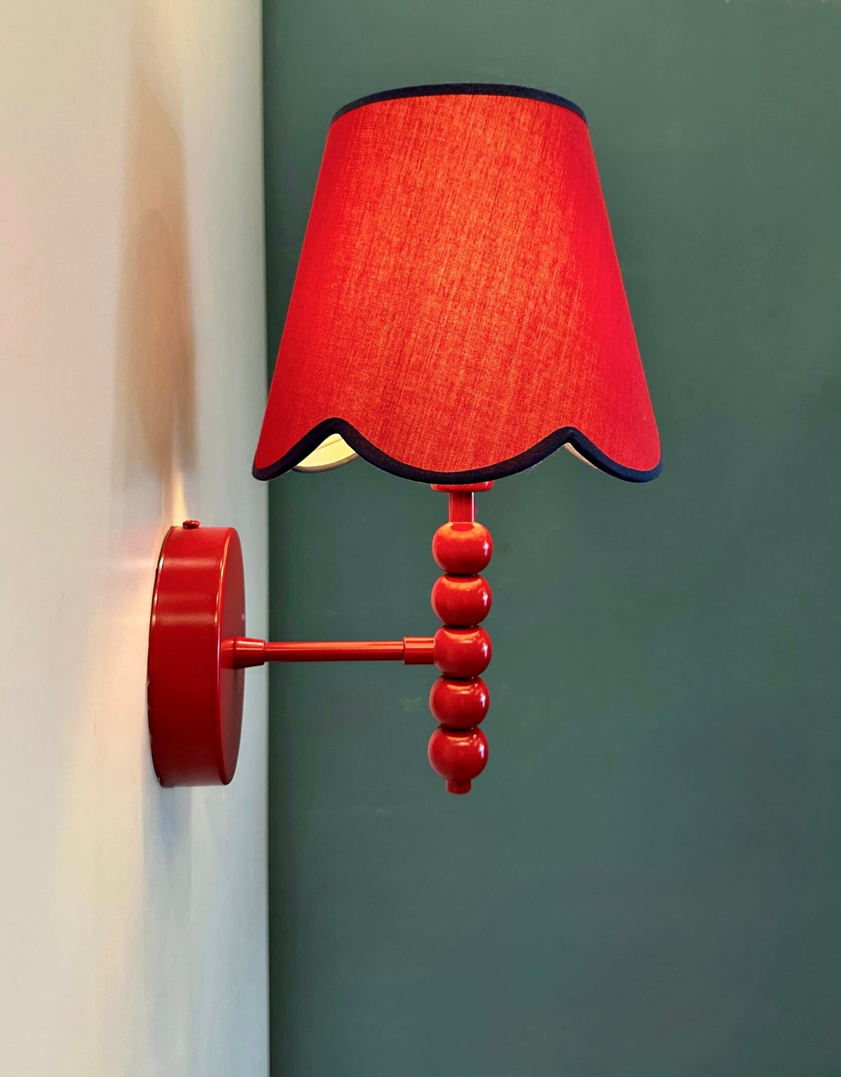PROMIN red wall sconce side view showing round wall plate, metal arm and beaded stem against a green wall