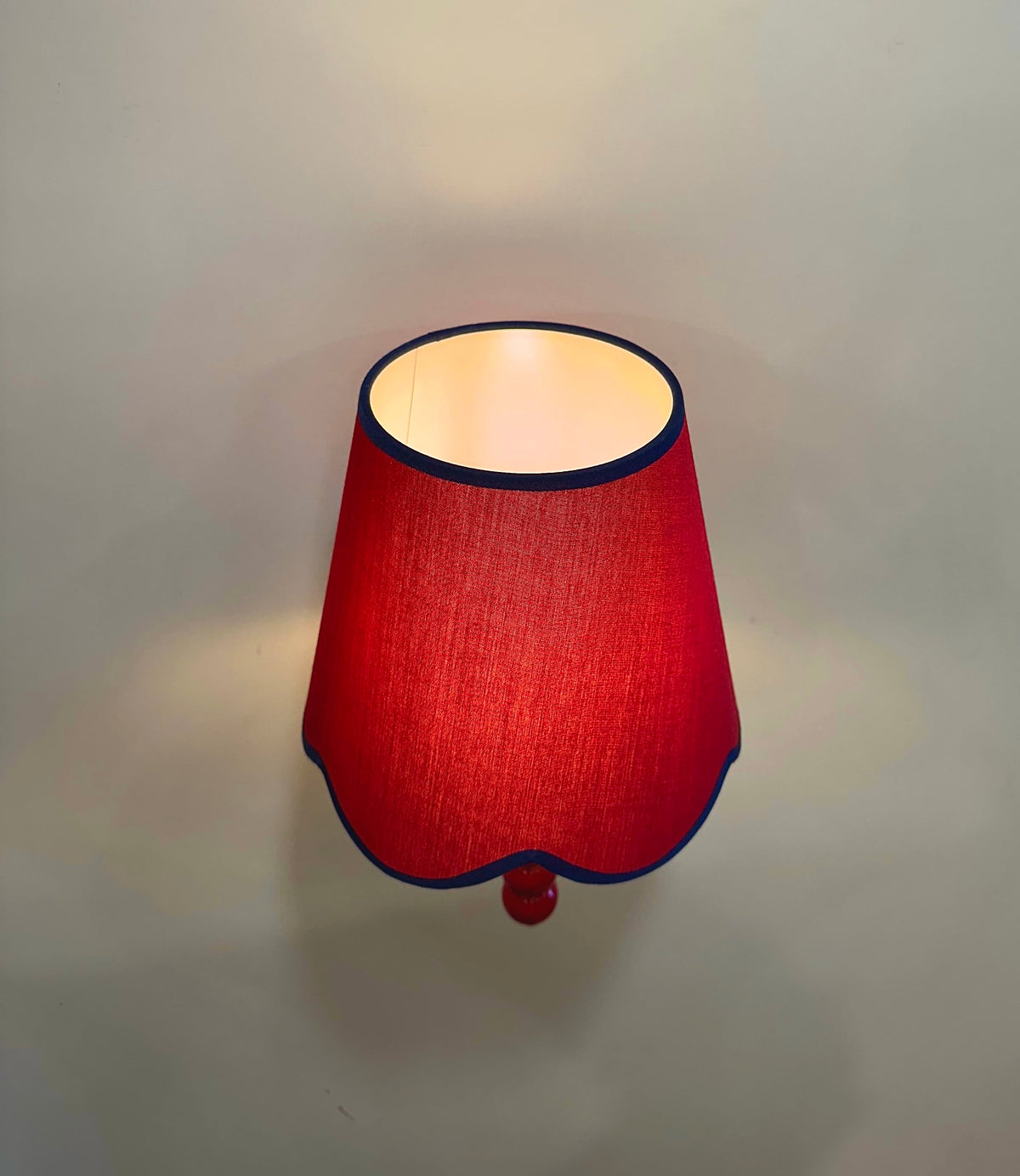 Top view of PROMIN red fabric lampshade with navy piping and white lining, lit on the wall