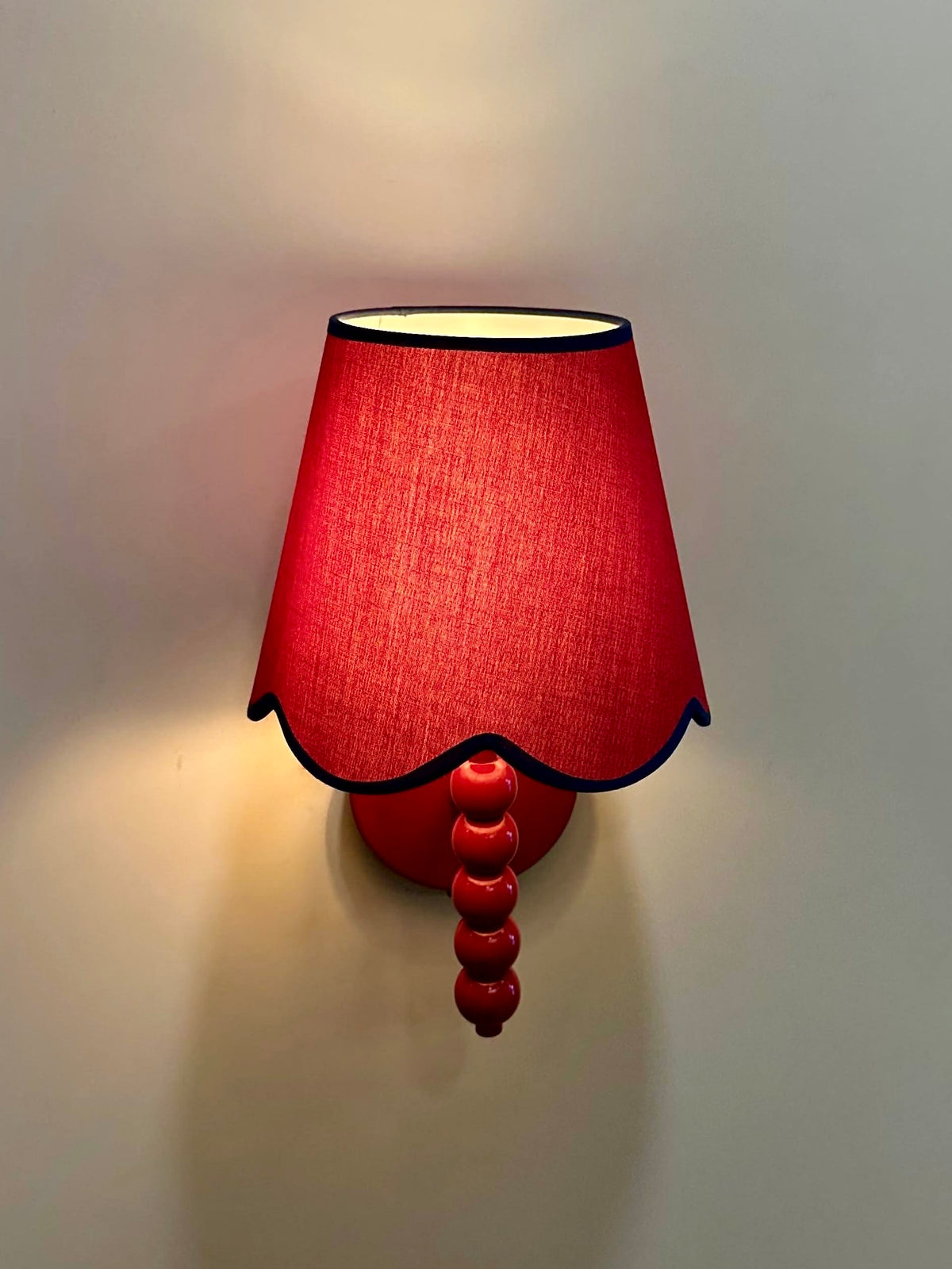 PROMIN red wall sconce front view, glowing scalloped fabric shade above a glossy red beaded stem