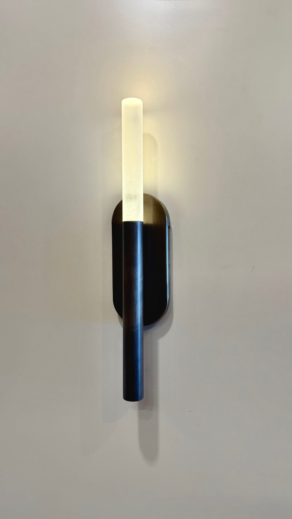 MUSALA modern wall sconce lit, with a glowing plexiglass diffuser above a slim vertical metal body