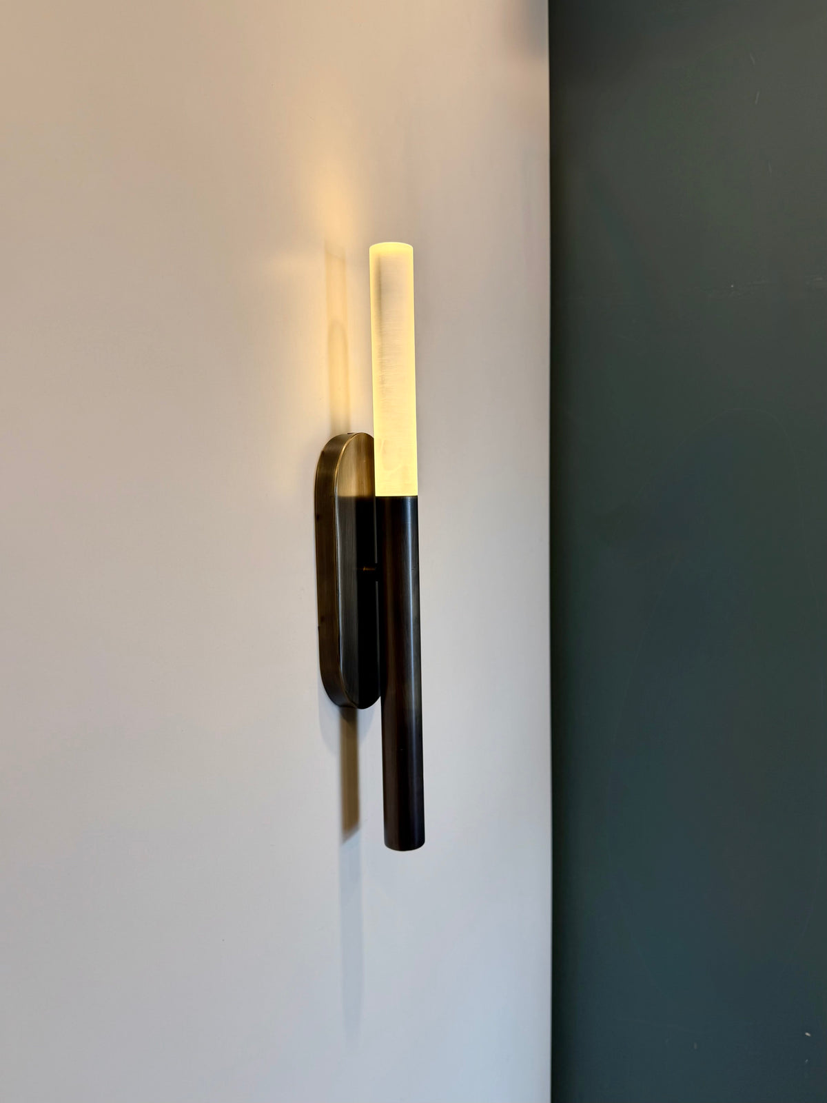 MUSALA modern wall sconce angled view beside a dark green wall