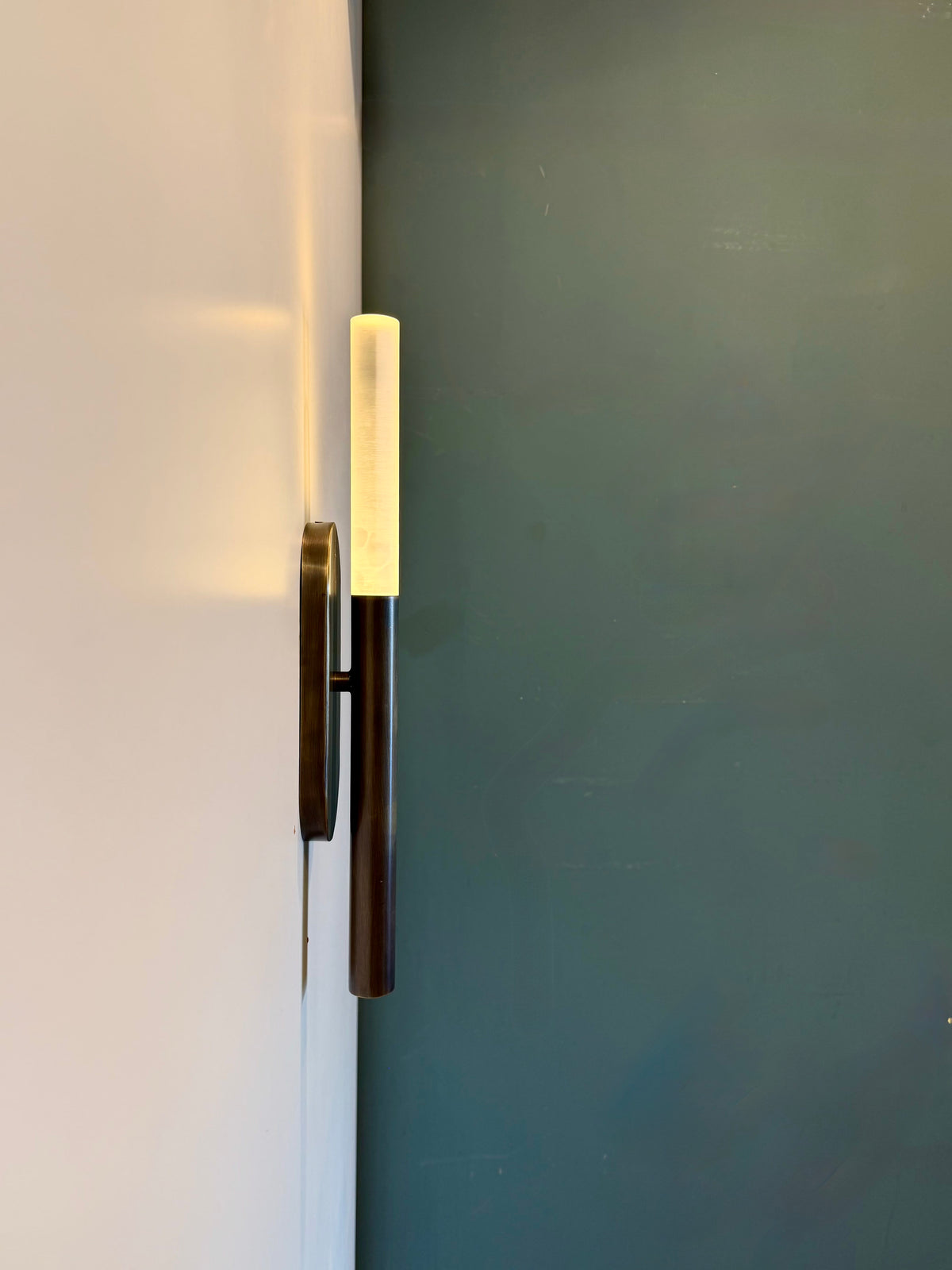 MUSALA wall sconce side view next to a dark green wall, showing its slim profile