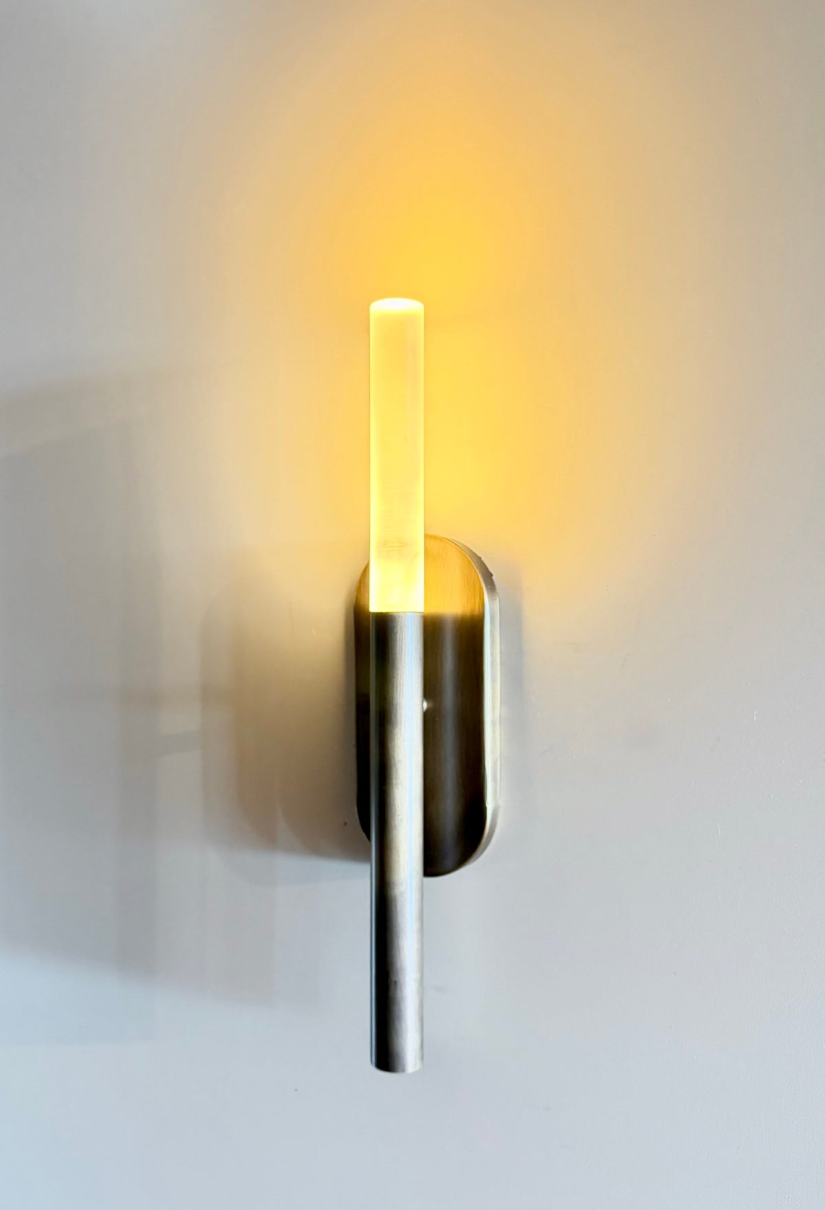 MUSALA modern wall sconce lit, warm light rising from the plexiglass diffuser