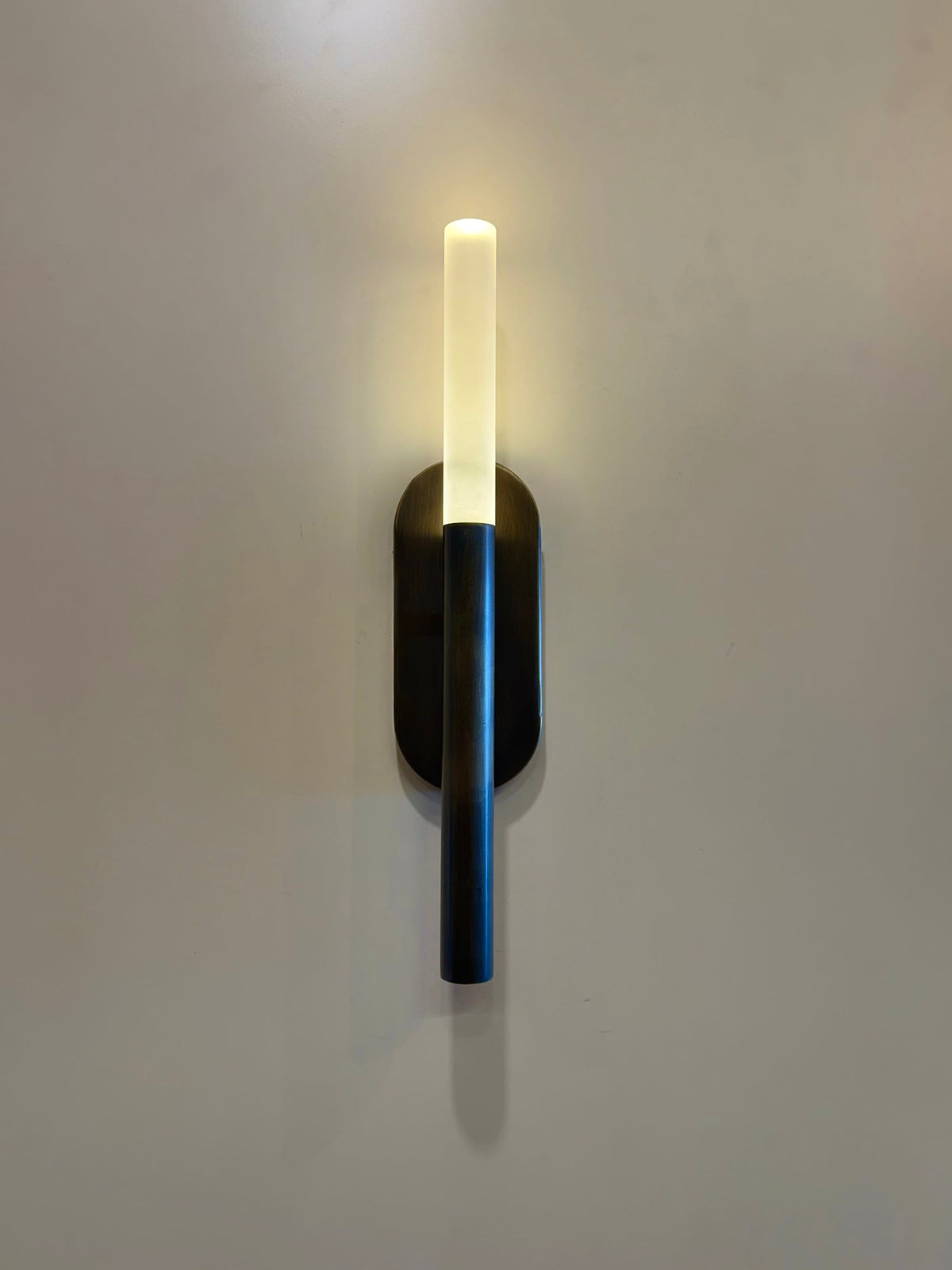 MUSALA vertical wall light front view with oval backplate and plexiglass tube