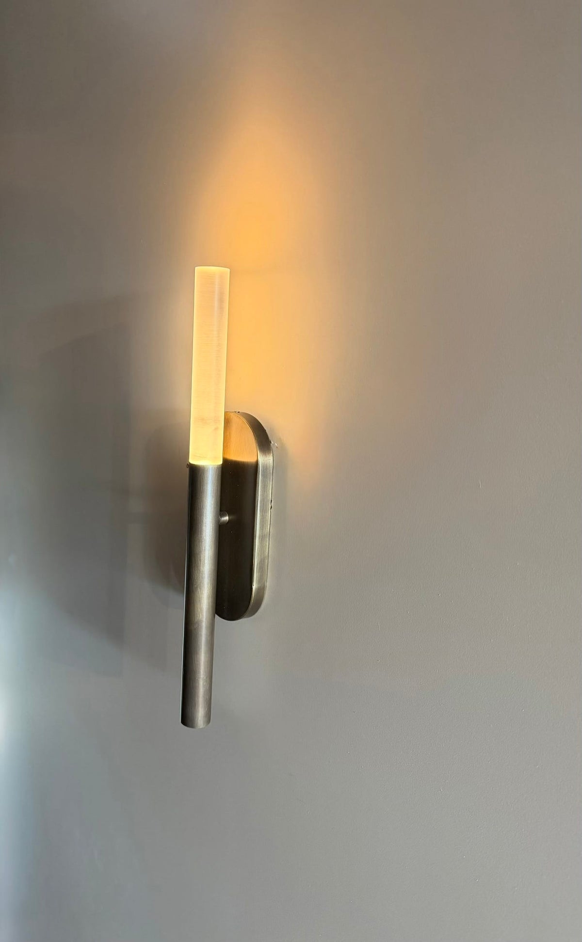 MUSALA minimalist wall sconce casting a warm glow upward on a beige wall