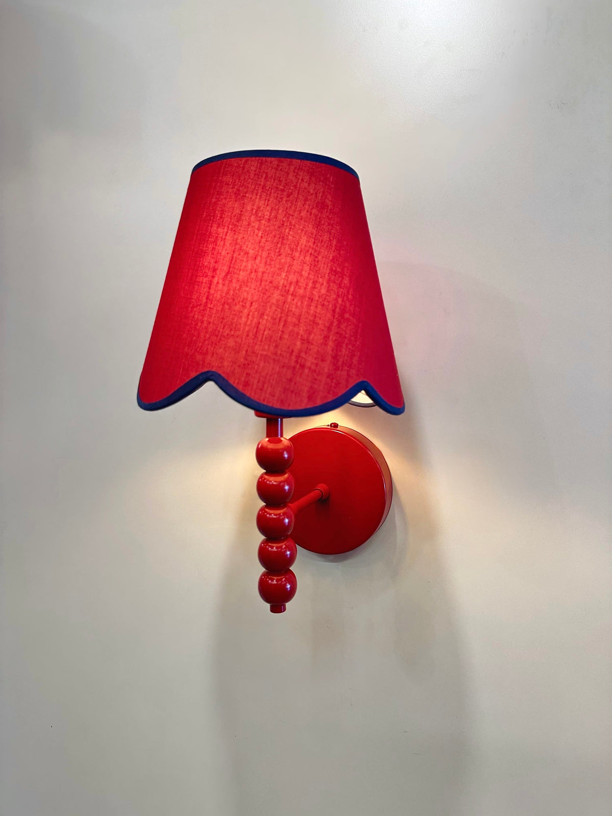 PROMIN red wall sconce three-quarter view, red fabric shade with scalloped navy-trimmed edge