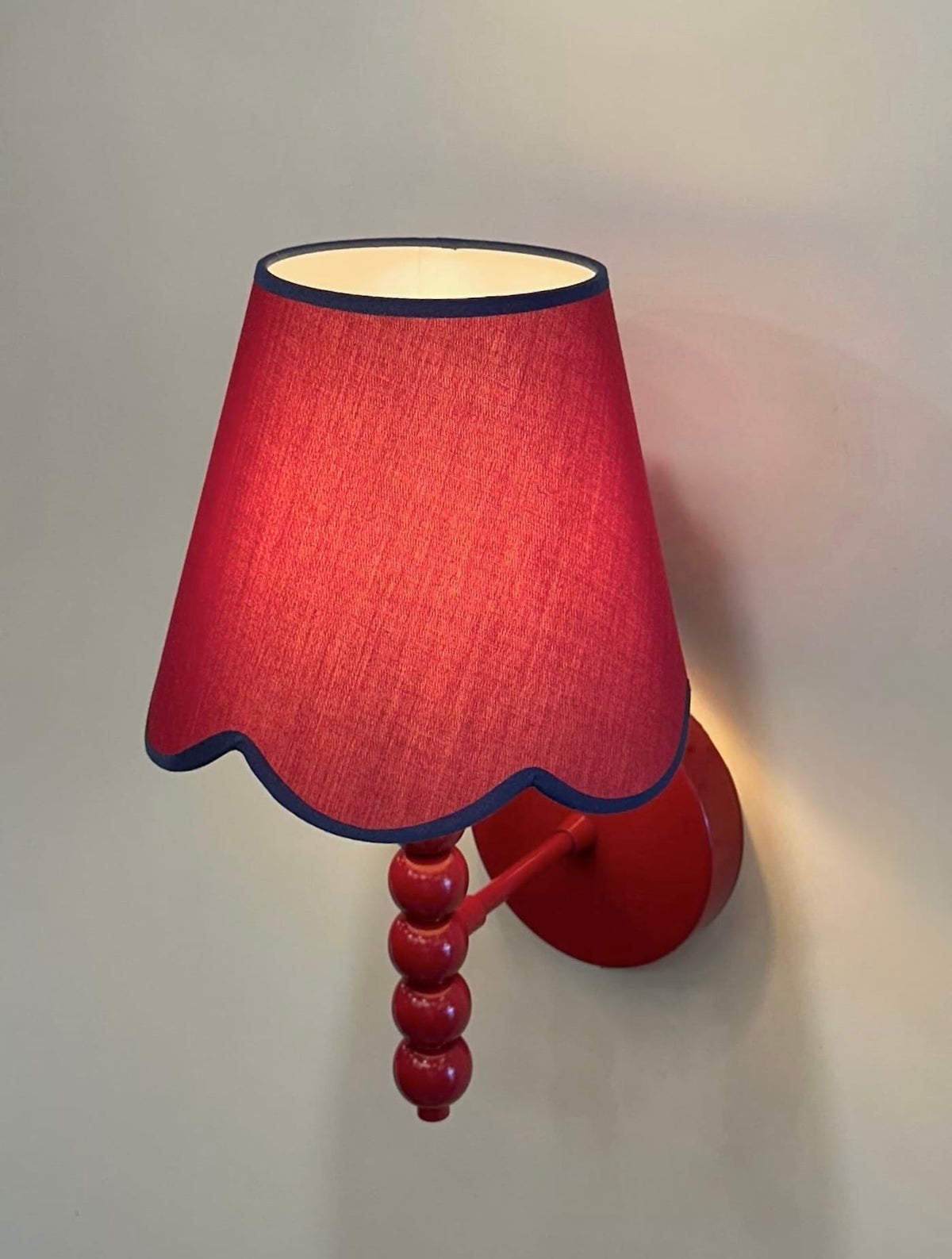 PROMIN red beaded wall sconce lit from a low angle, showing shade, beads and wall plate